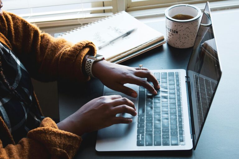 Close-up of a person typing on a laptop indoors with a coffee mug nearby, ideal for remote work themes.